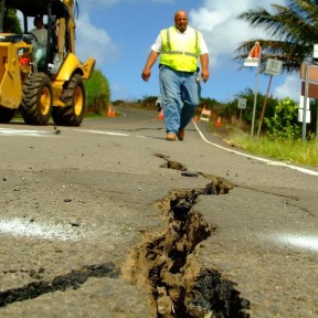 Crack in the road after an earthquake. Man walking and tractor in background.