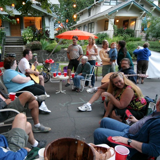 Neighbors sit in lawn chairs and stand around during a block party. 