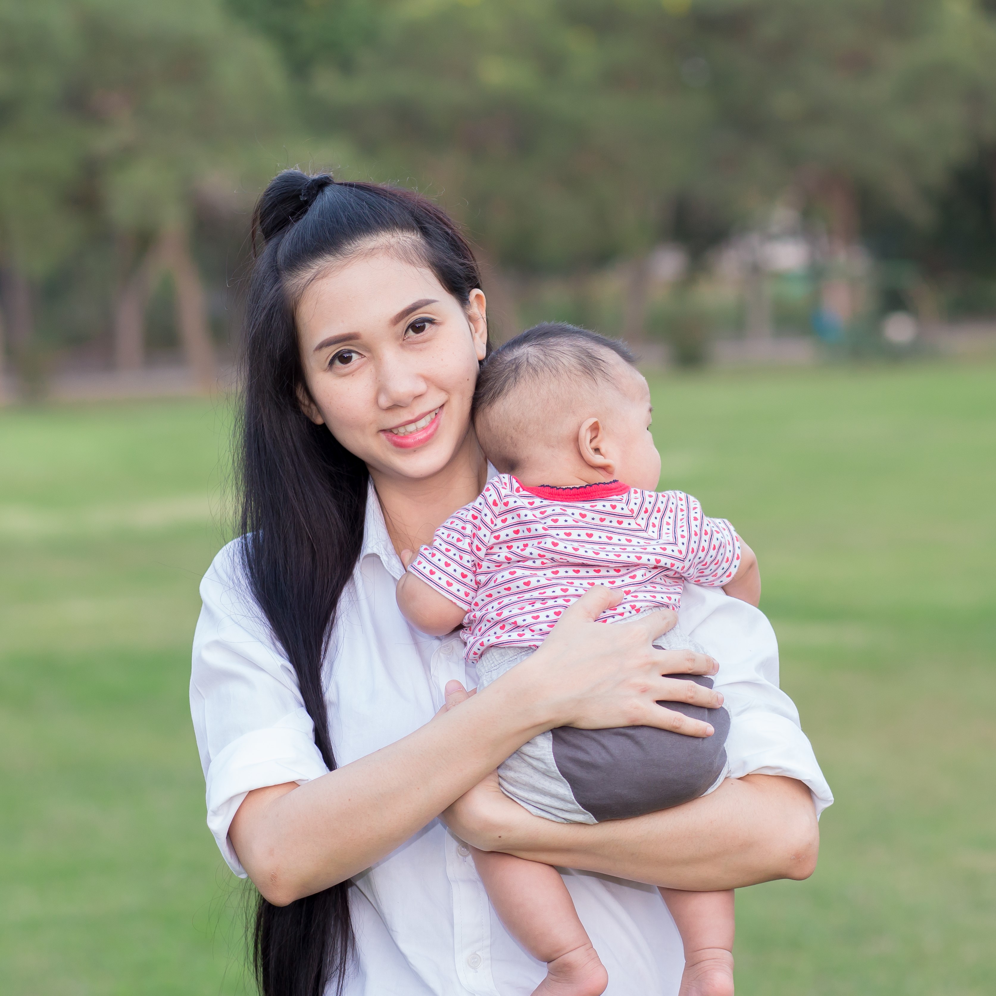 Smiling woman holding baby. Woman appears to be Asian American. 