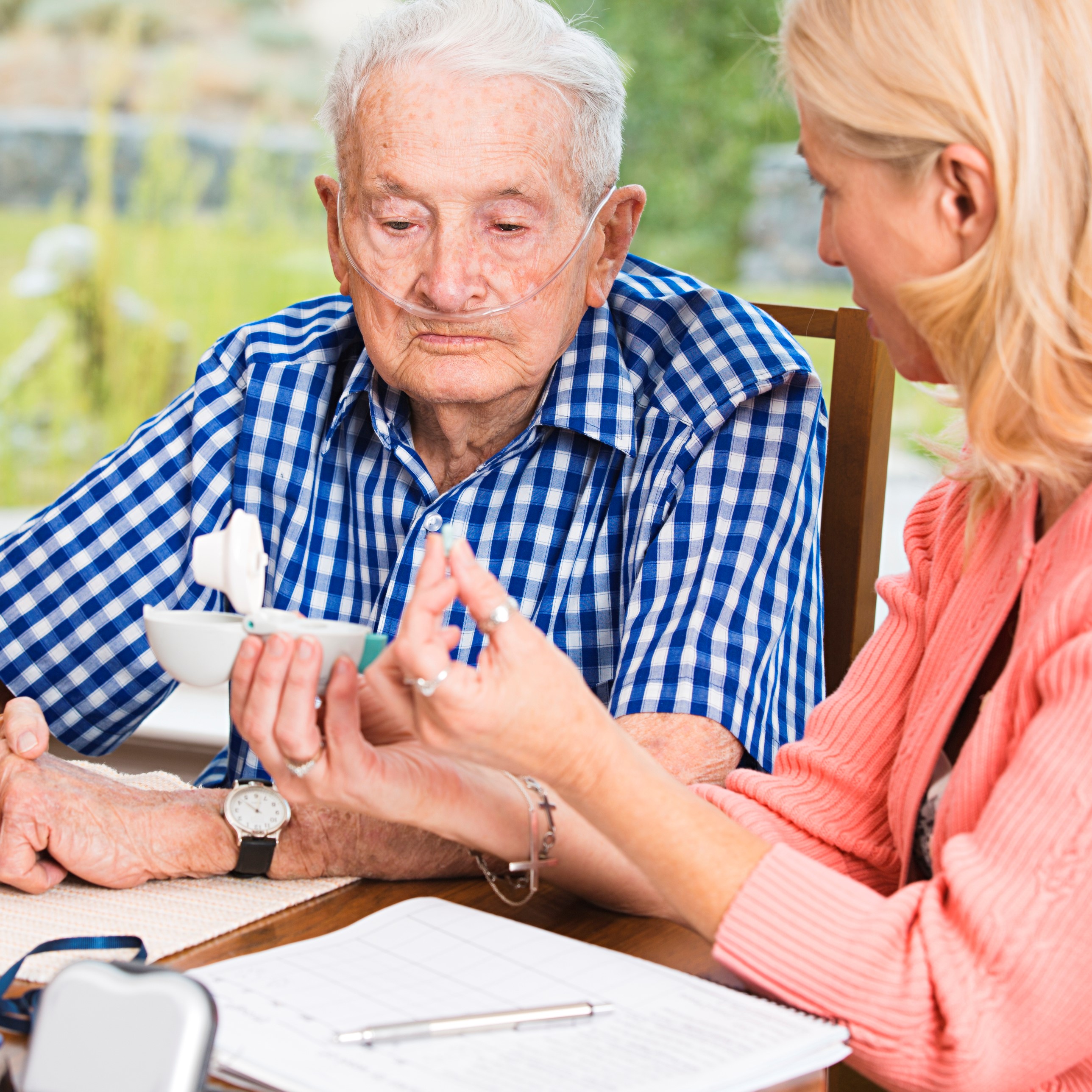Elderly man sits at a table with a woman. She is showing him the details of his medication.