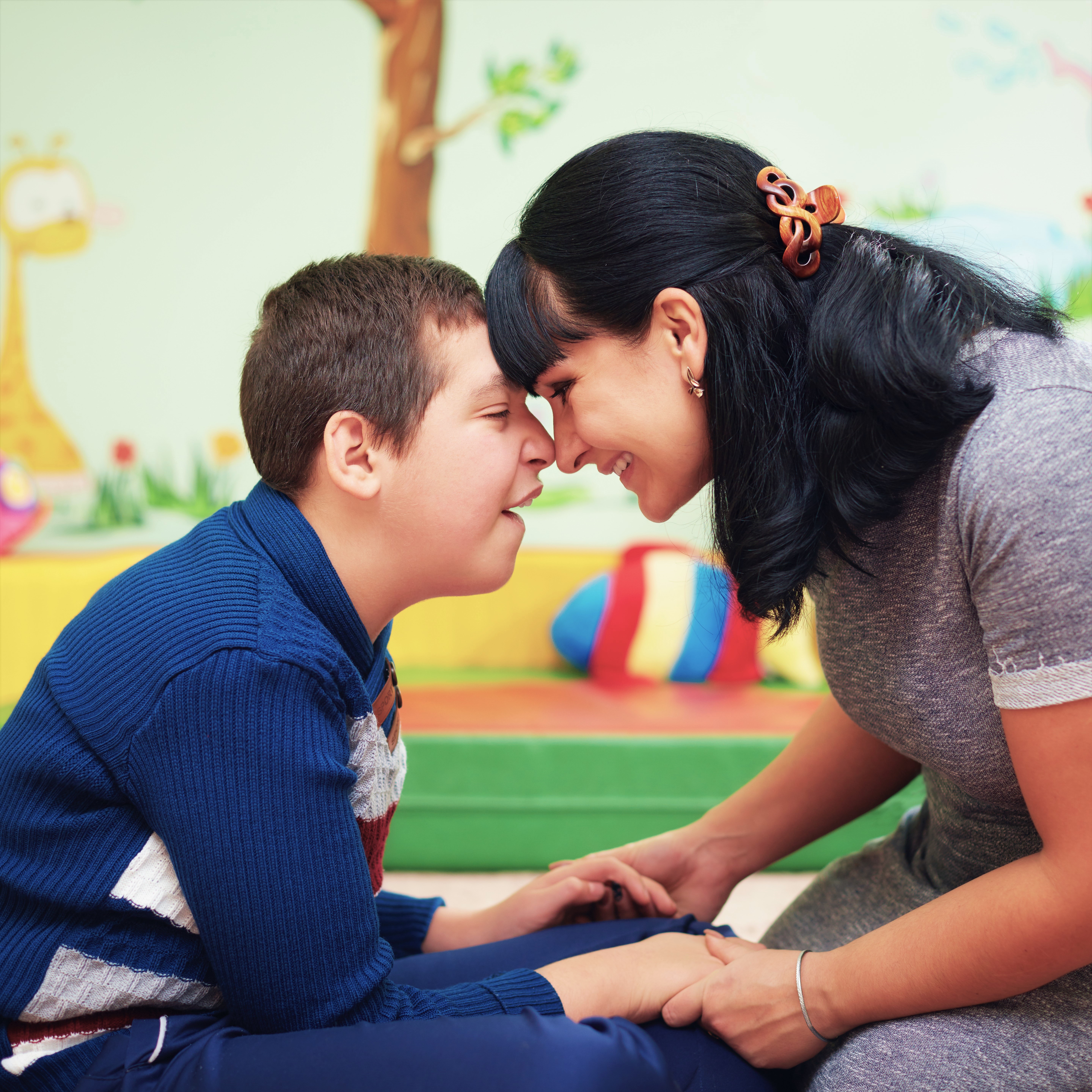 Child with cognitive disability touches his forehead to a woman's forehead. They are both smiling and seem very happy.