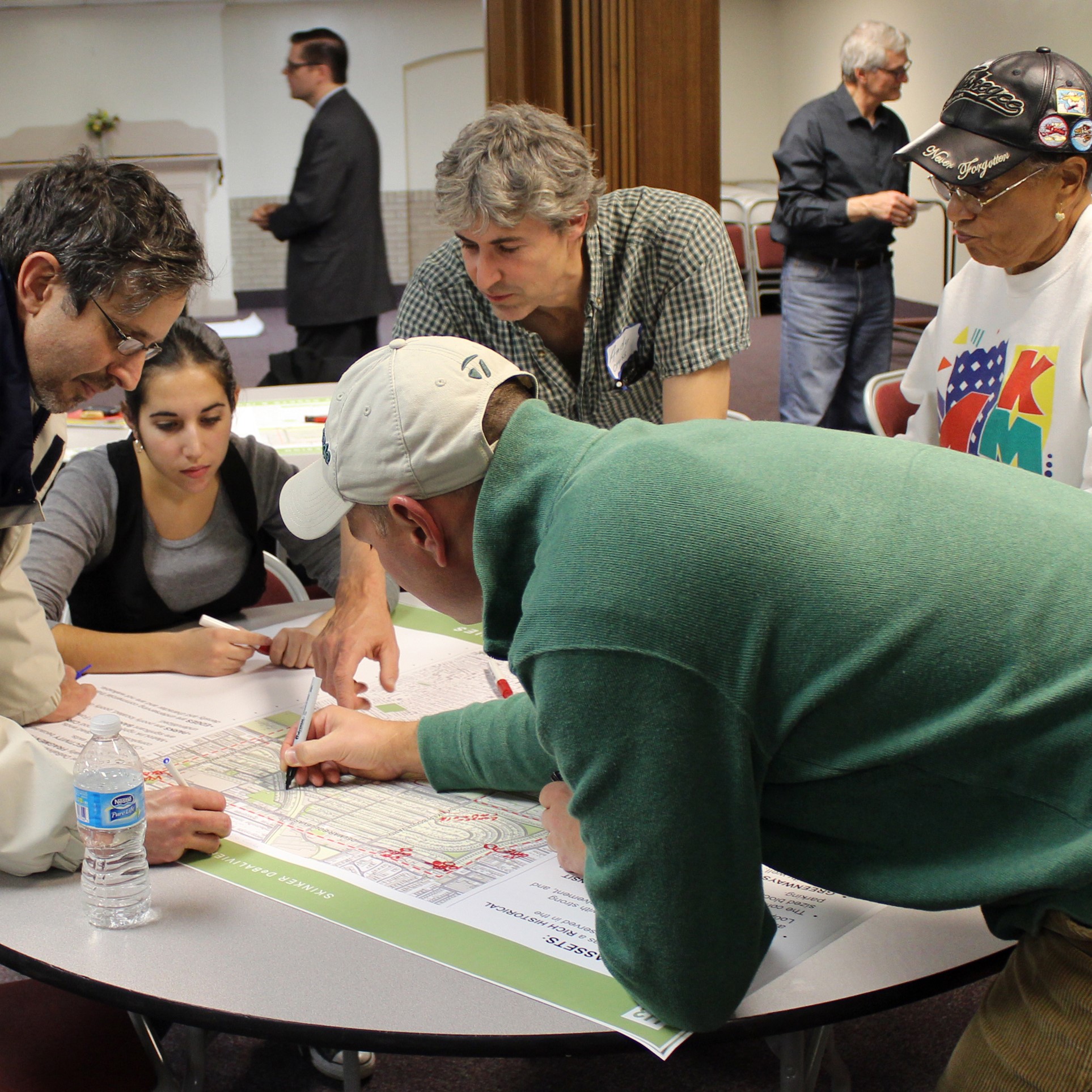 Community members make plans for their neighborhood. Med and women are standing around a table looking at a map. 