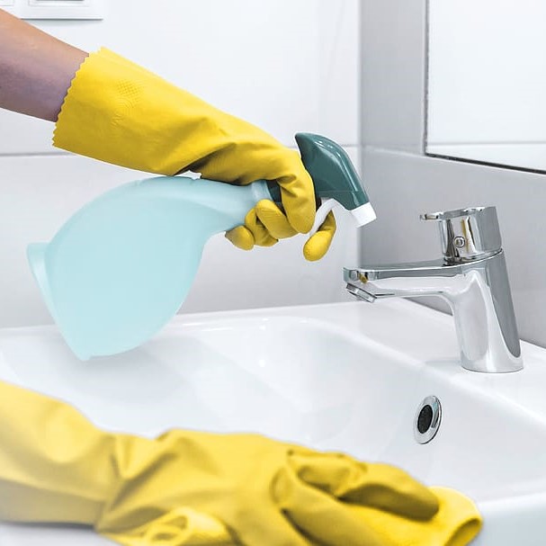 Gloved hands spray cleaner on bathroom sink